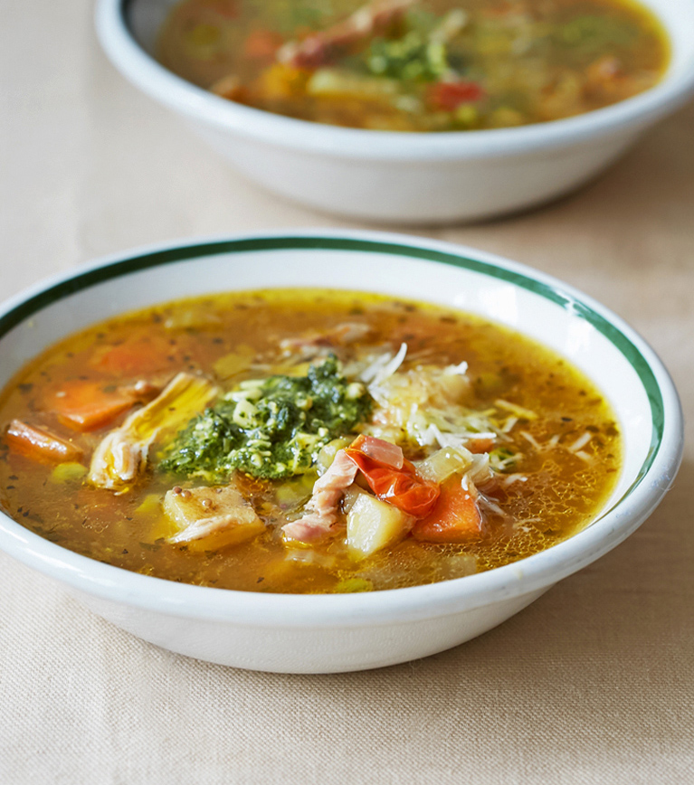 A bowl of chicken parmesan soup topped with green pesto 