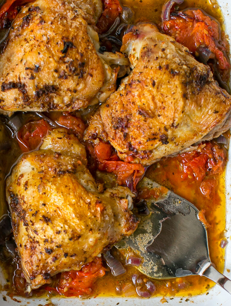 Oven roasting tray filled with Garam Masala Roasted Chicken and spoon scooping up spiced oil. 