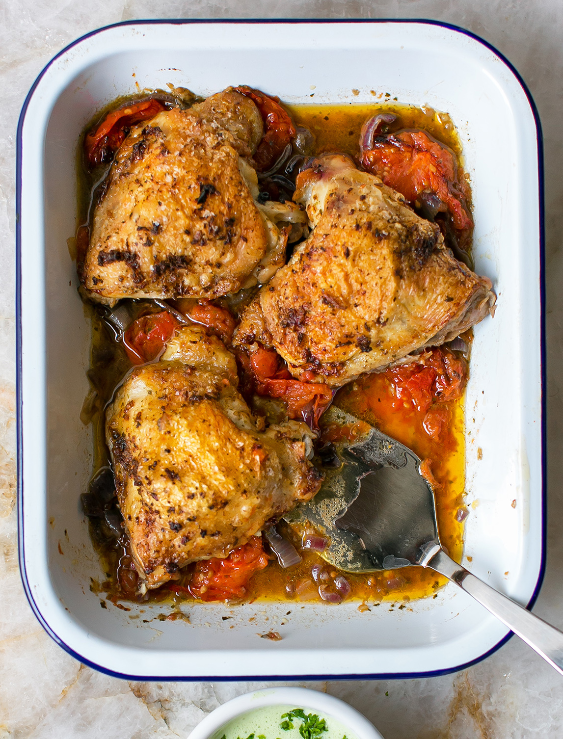 Oven tray with Garam Masala Roasted Chicken Recipe inside and spoon for scooping up spiced oil