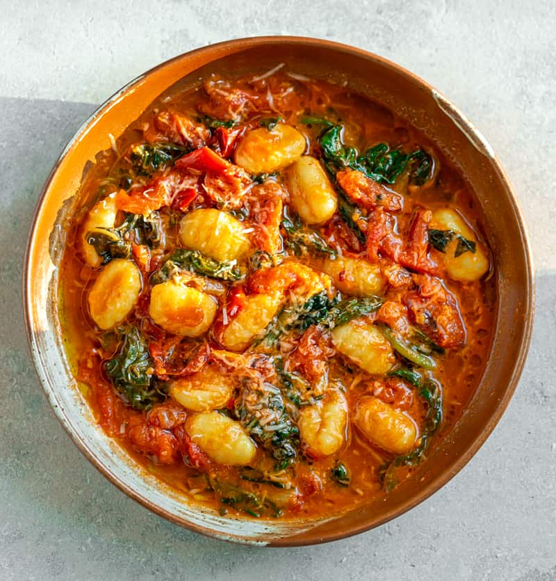 gnocchi with swiss chard and roasted tomato parmesan sauce in a brown ceramic bowl