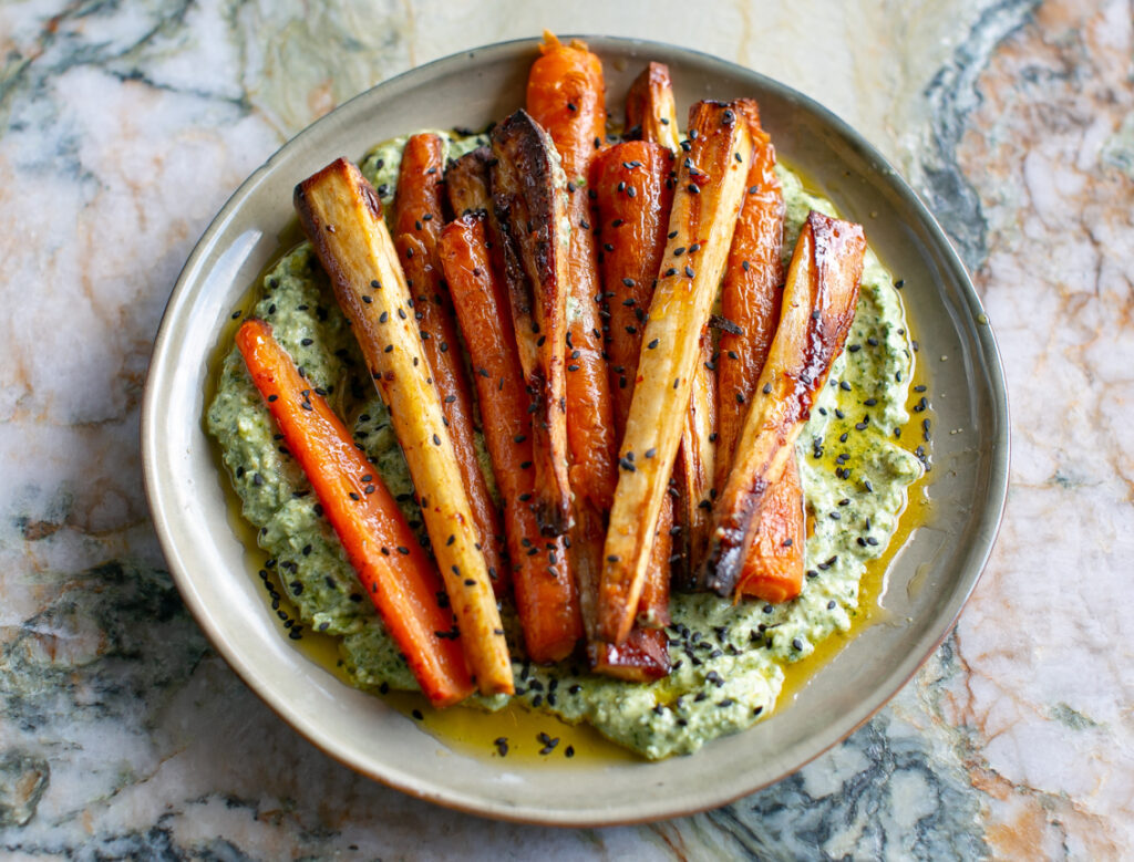 Beige ceramic plate filled with  Charred Green Feta Sauce and topped with harissa honey glazed carrots