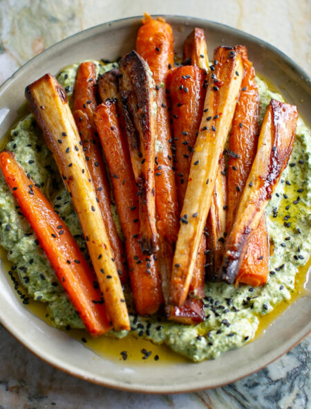 Beige ceramic plate filled with Charred Green Feta Sauce and topped with harissa honey glazed carrots