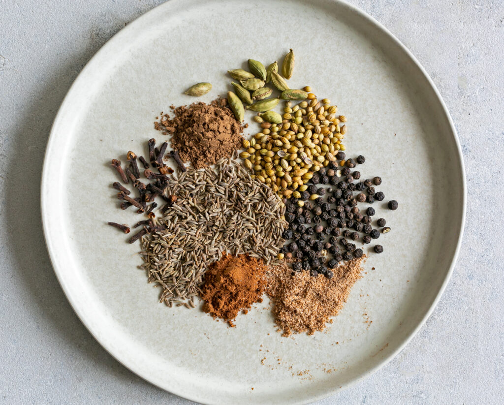 beige ceramic plate showing a mix of spices used to make Baharat spice blend