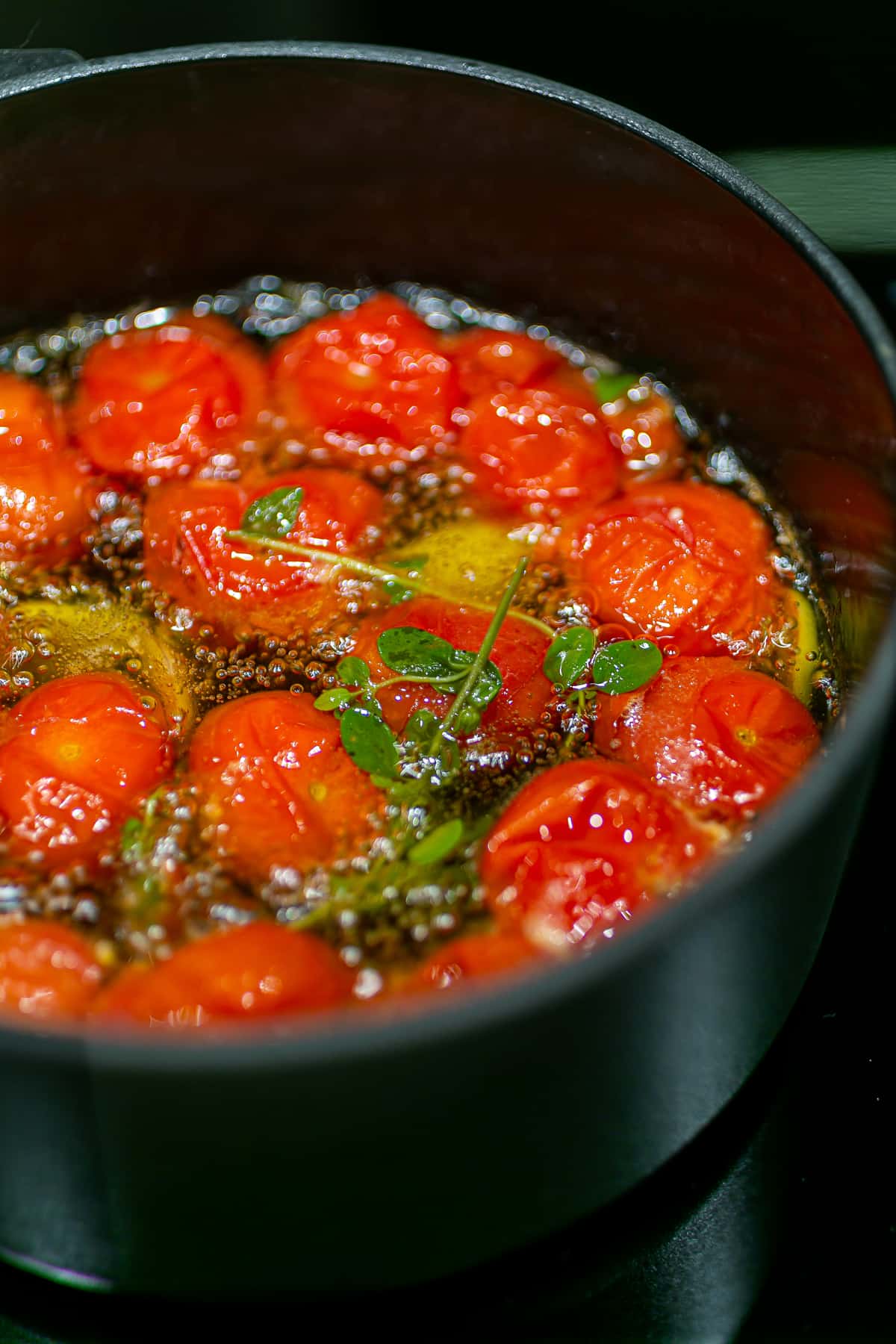 a black saucepan with bright red cherry tomatoes bubbling in olive oil