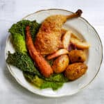 Roasted chicken leg with cabbage, carrots, roasted potatoes and apple gravy in a vintage porcelain bowl on a white wooden table