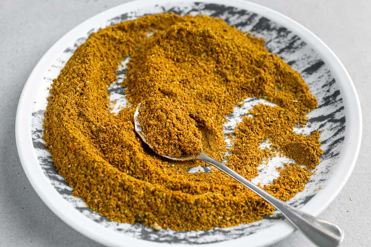 A plate with bright mustard coloured homemade Madras Curry Powder Blend and a spoon