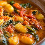 gnocchi with swiss chard and roasted tomato parmesan sauce in a brown ceramic bowl