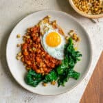 Beige ceramic plate on a beige ceramic table with spicy Italian 'Nduja beans, spinach and a crispy fried egg with bright yellow yolk