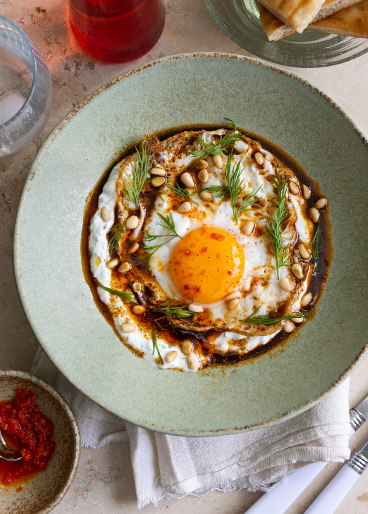 Herb yoghurt with a fried egg on top, chilli oil and dill in a green ceramic bowl