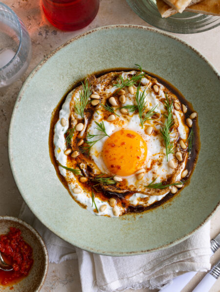 Herb yoghurt with a fried egg on top, chilli oil and dill in a green ceramic bowl