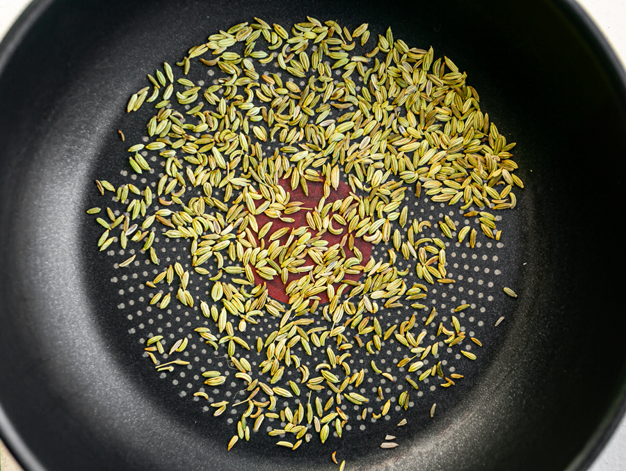whole fennel seeds being roasted in a frying pan