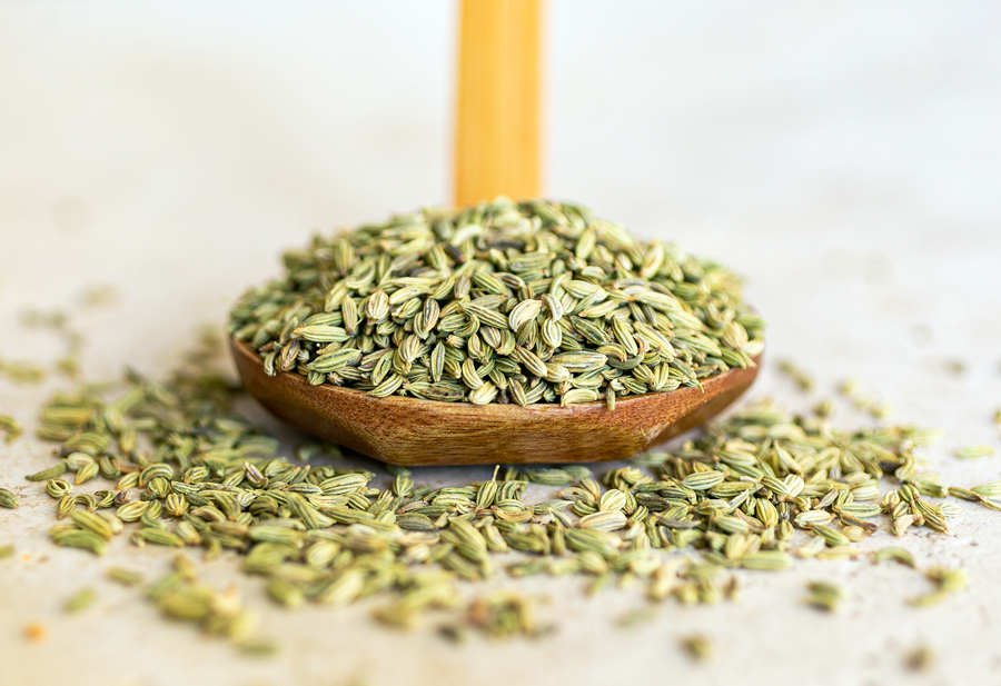 whole fennel seeds on a wooden spoon spilling onto the table