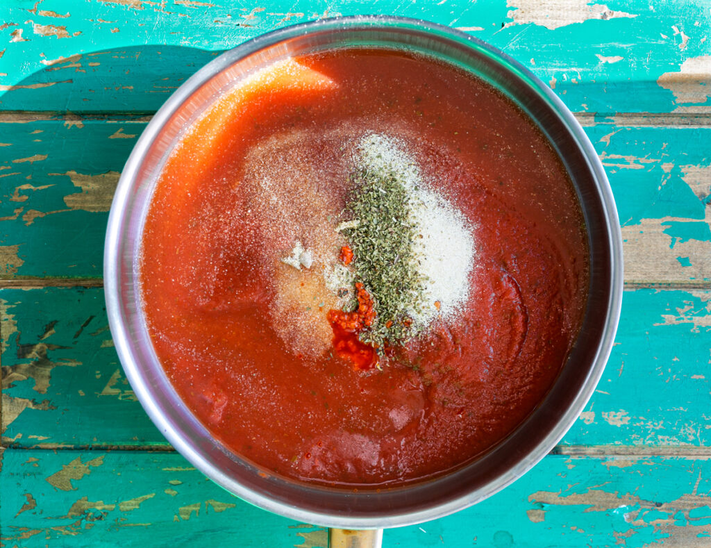 Pan of tomato sauce with seasonings resting on a blue wooden table