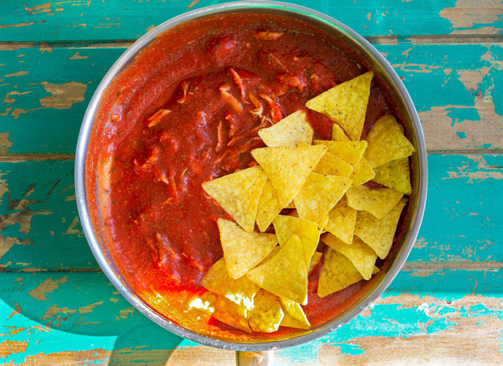 a pan of chilaquiles tomato sauce with tortilla chips