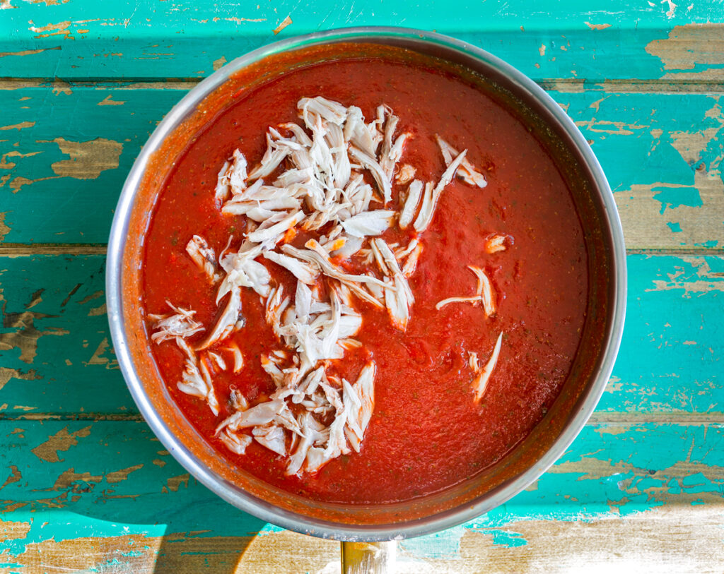 a pan of chilaquiles tomato sauce with shredded chicken