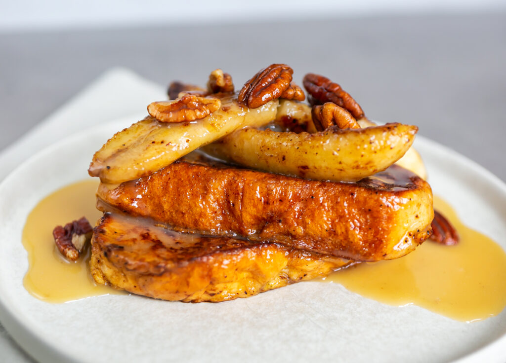 Maple Cardamom Butter French Toast topped with banana, pecans and with oozing sauce