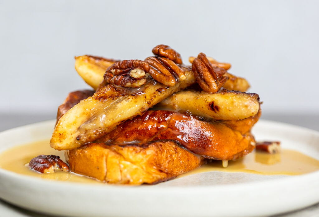 Maple Cardamom Butter French Toast topped with banana, pecans and with oozing sauce