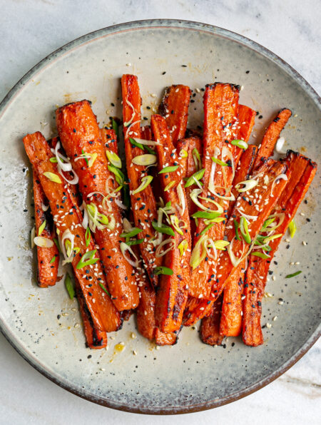 Blue ceramic plate with miso sesame roasted carrots on top garnished with black sesame seeds and sliced spring onion