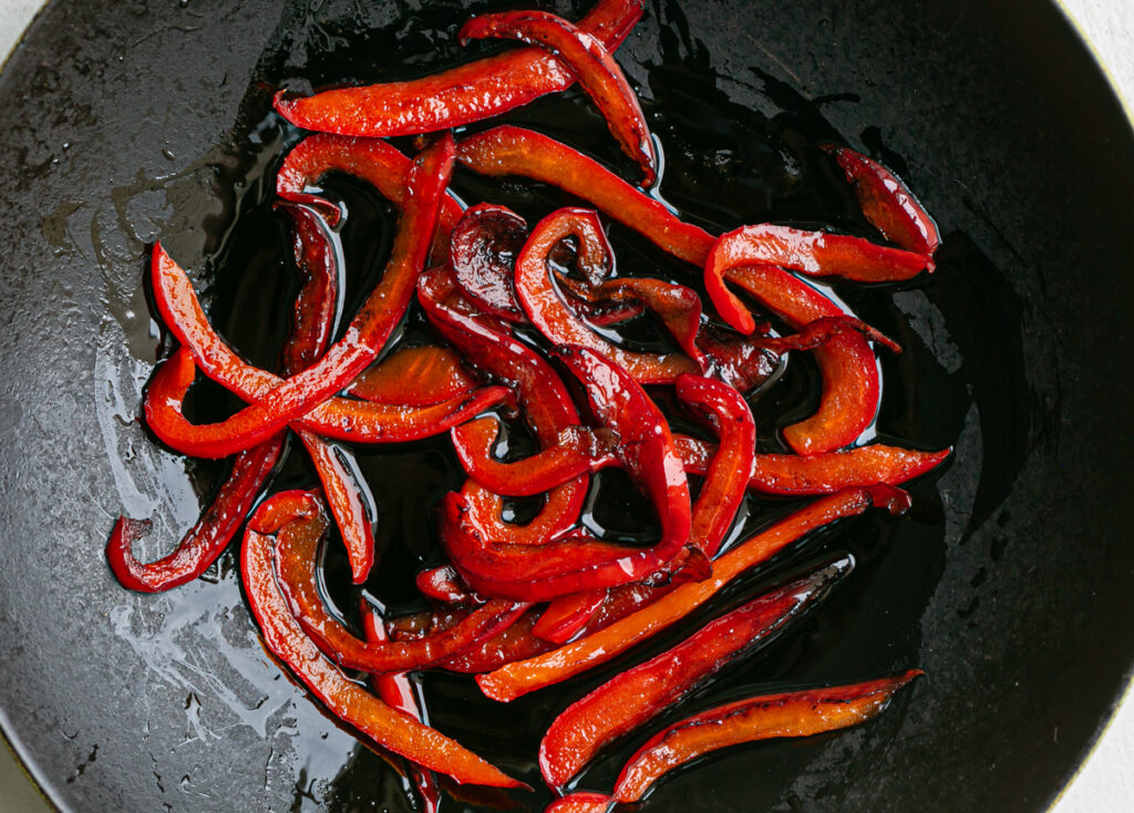 Slices of red pepper frying in a pan