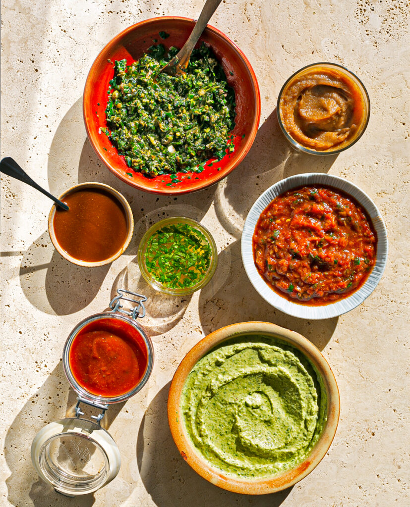 Bright sun shinning on a stone table of small coloured bowls filled with different sauces