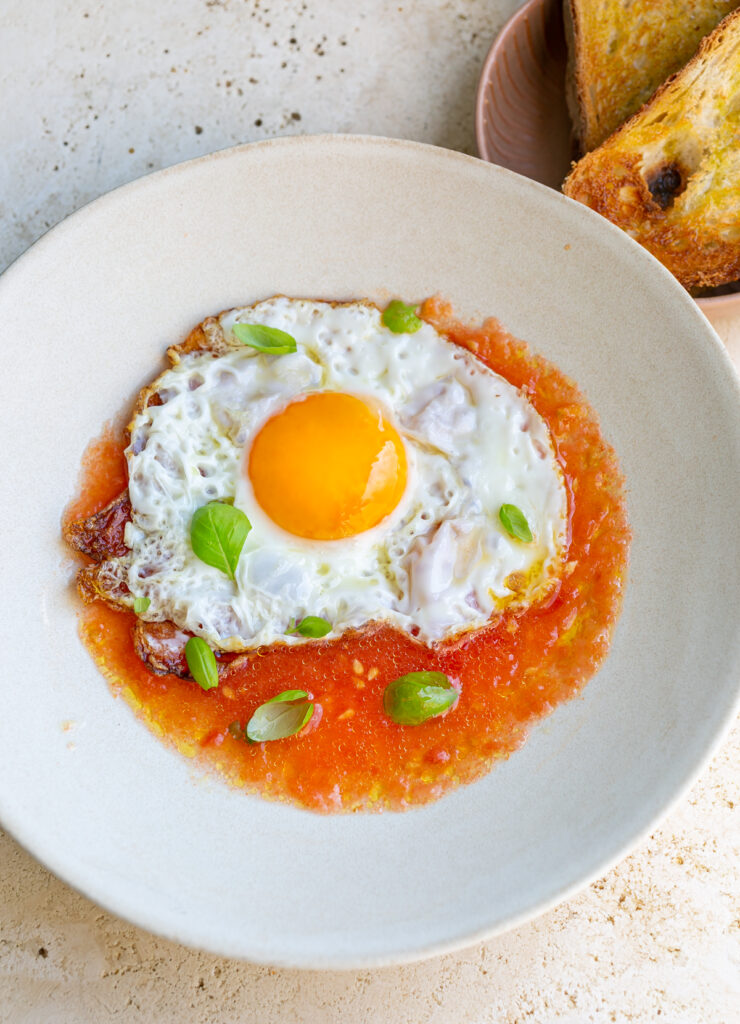 Beige ceramic bowl filled with fresh grated tomato salsa topped with a fried egg and a side serving of crusty toasted bread