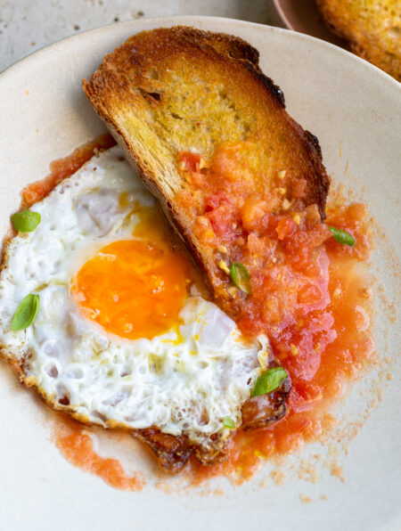 Beige ceramic bowl filled with fresh grated tomato salsa topped with a fried egg and a side serving of crusty toasted bread
