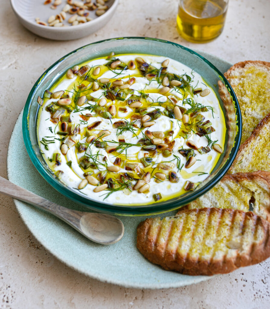 Blue bowl filled with creamy Creamy Yoghurt Feta Whip topped with pine nuts on a green plate with toasted bread