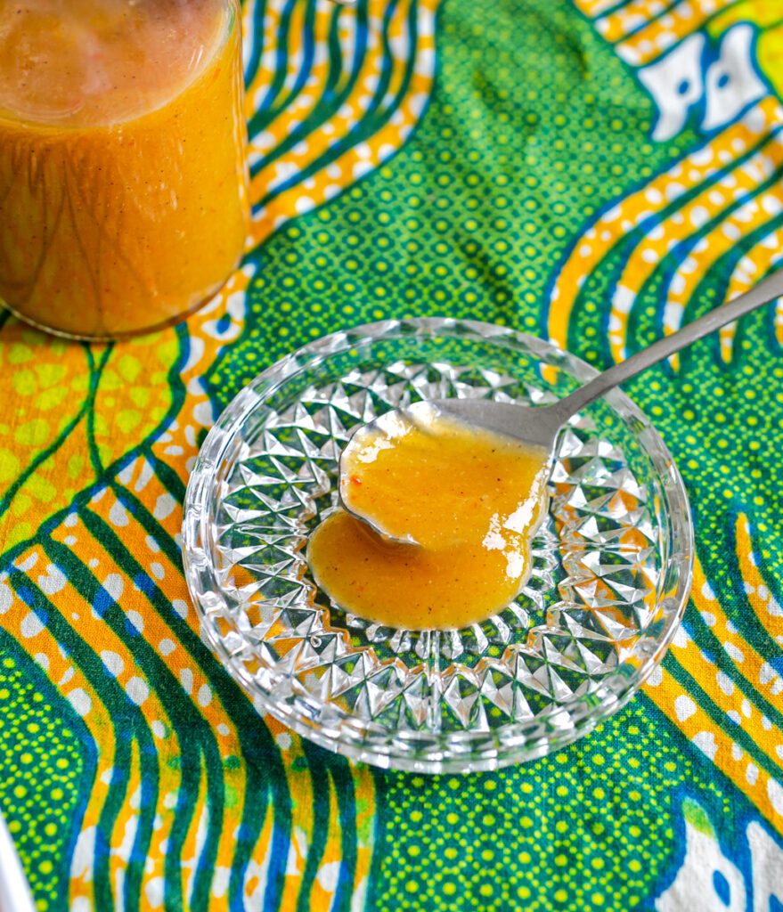 small glass bowl with a spoon of orange habanero mango hot sauce