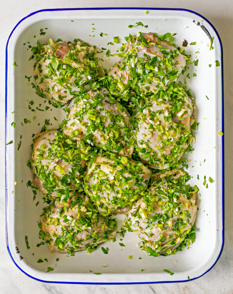 Oven roasting tray with chicken thigh fillets marinated in oil, garlic and fresh green herbs