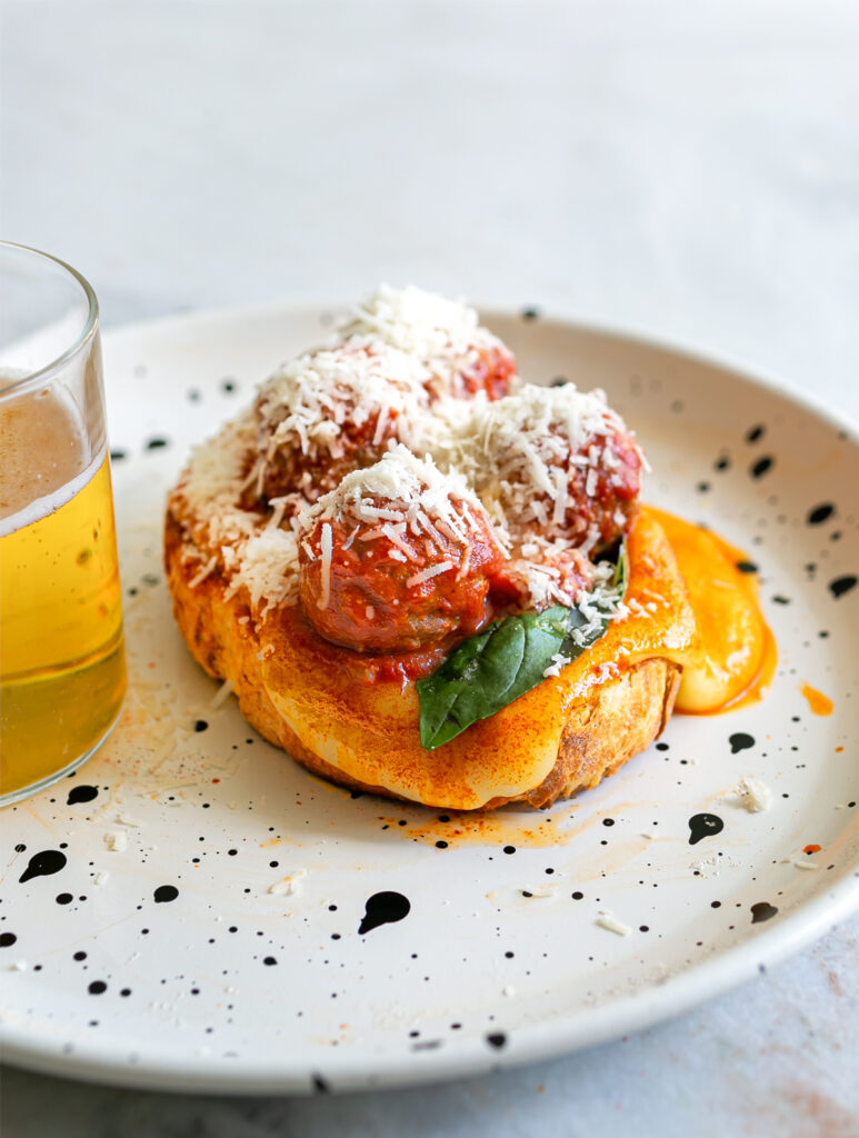 Toast topped with melted fondue cheese sauce, basil, meatballs in tomato sauce, grated parmesan and a beer