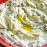 Small red ceramic bowl filled with pickle tzatziki and a drizzle of olive oil