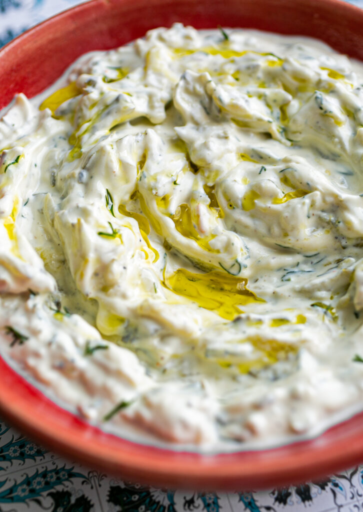 Small red ceramic bowl filled with pickle tzatziki sauce and a drizzle of olive oil