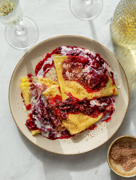 beige ceramic plate with Crepes with Spiced Plum Rum Compote and a bottle of prosecco