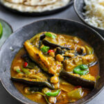Grey ceramic bowl filled with Fragrant Aubergine Coconut Curry next to rice and flatbreads