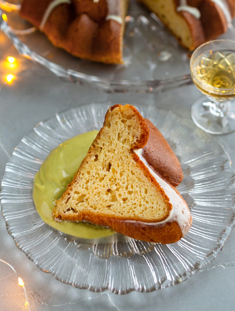 a slice of Rum Baba Cake with pistachio cream on a glass plate and a glass of brandy