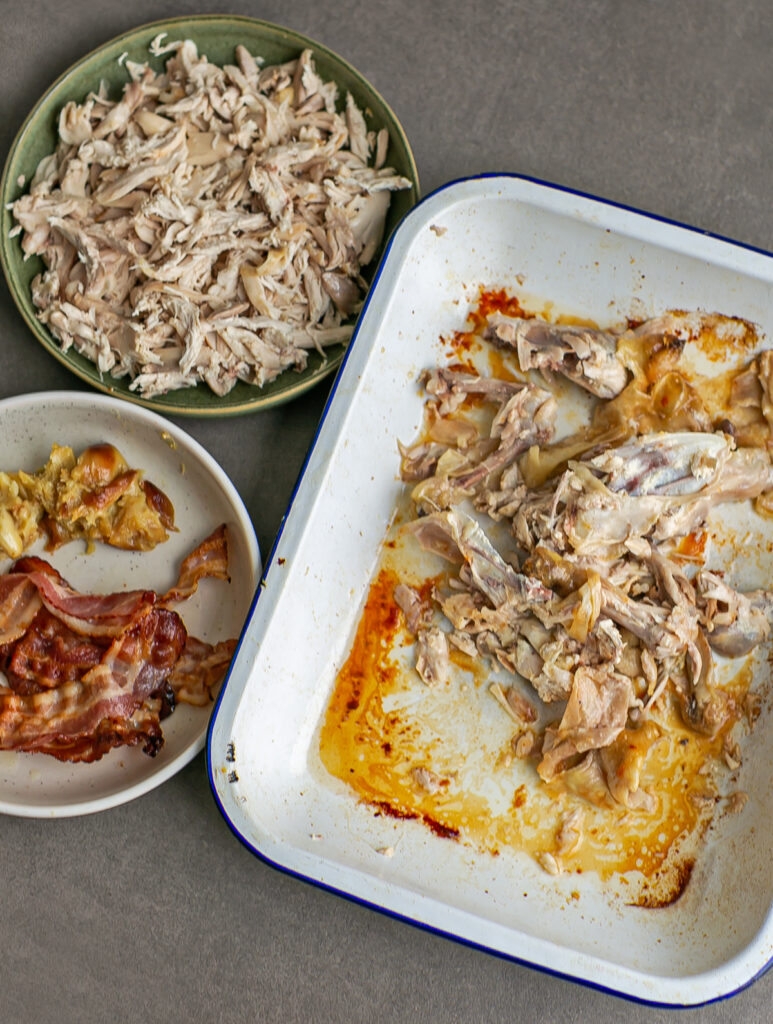 Chicken meat alongside bones, roasted garlic and bacon