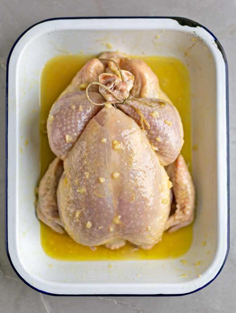 a whole raw chicken marinating on oil, vermouth and garlic