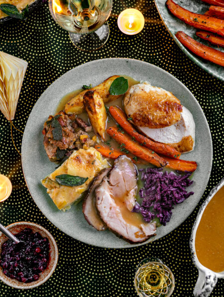 A plate with The Ultimate Christmas Dinner, roast chicken and pork, glazed carrots, potatoes and red cabbage with chicken gravy